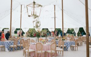 A 60 ft wide sailcloth tent is adorned with gold chandeliers and white drapes gathered identically at each tent side pole