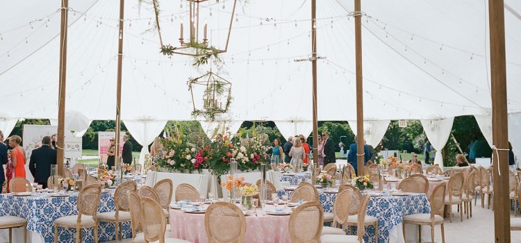 A 60 ft wide sailcloth tent is adorned with gold chandeliers and white drapes gathered identically at each tent side pole
